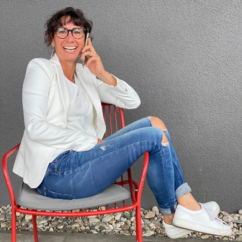 Claudia Potschigmann sitzt auf einem Stuhl und lacht während eines Telefonats mit einer Kundin.